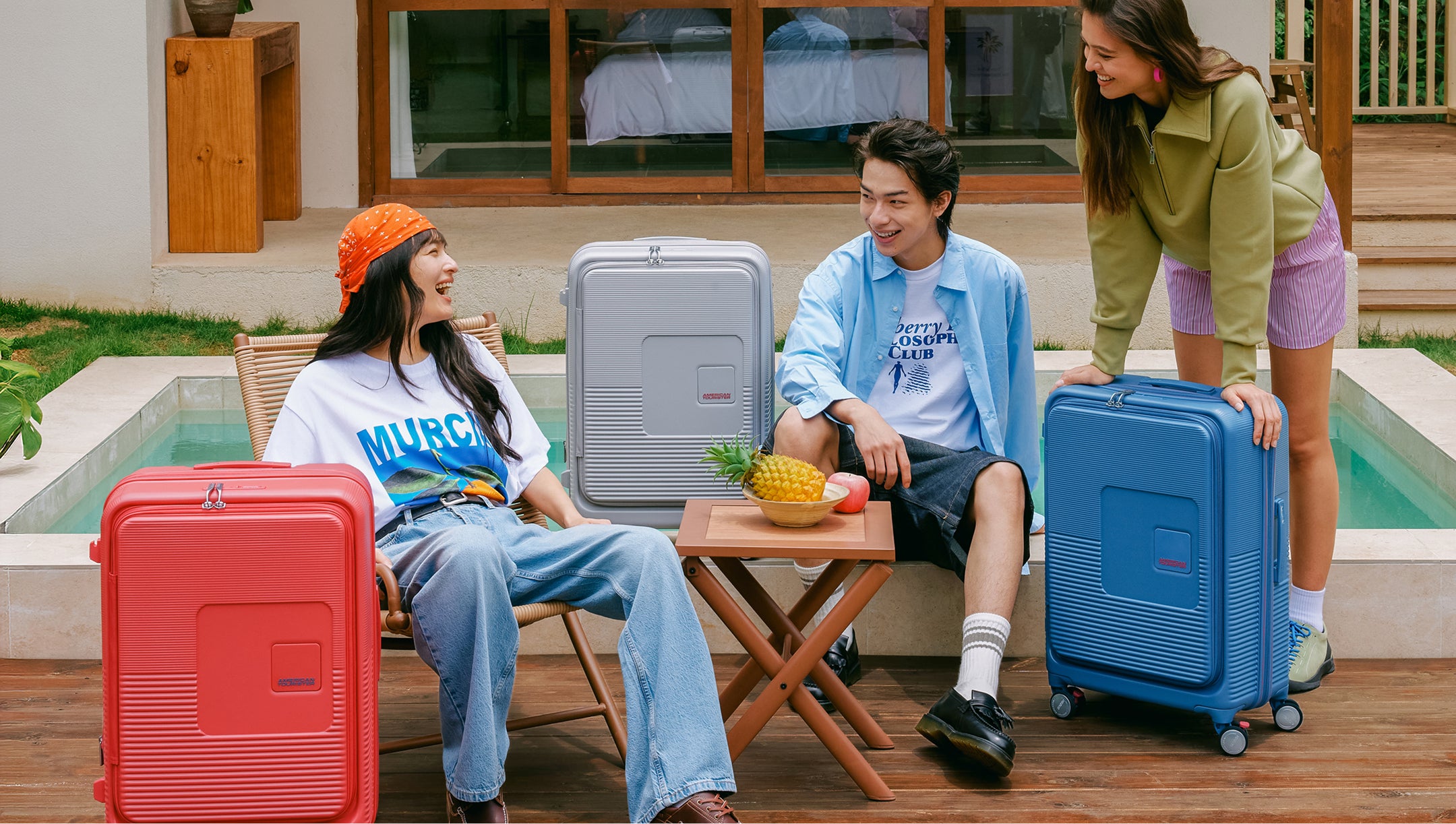 Three travellers with American Tourister luggage by a pool